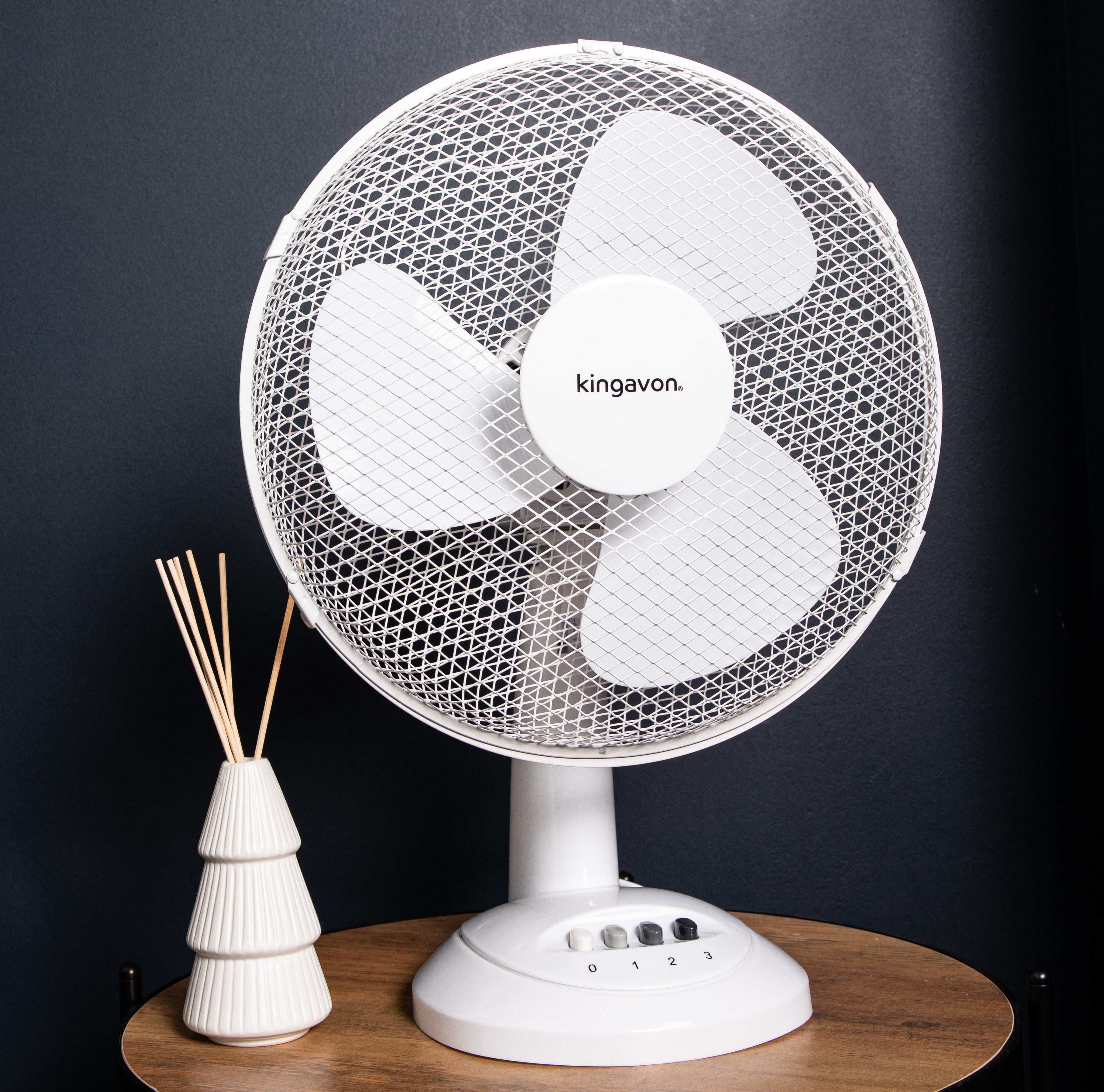White 30cm oscillating electric desk fan with a mesh grille and three blades, positioned beside a decorative white vase with reed sticks on a wooden table.