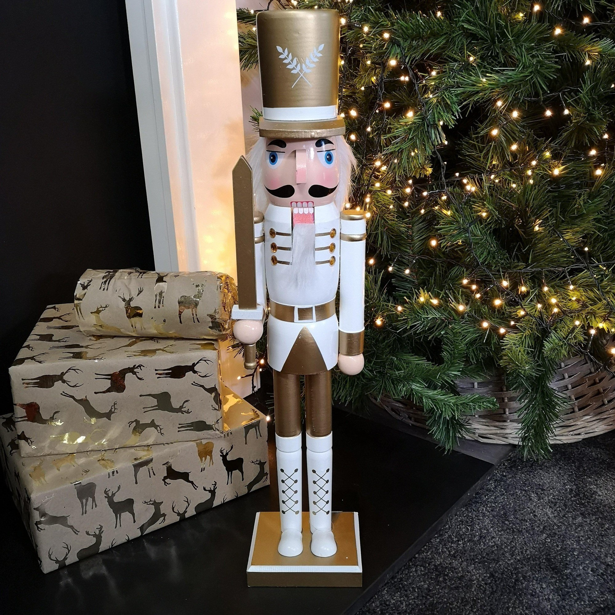 60cm wooden Christmas nutcracker soldier with a white body and shoes, gold accents, holding a sword, standing beside wrapped gifts and a decorated tree.