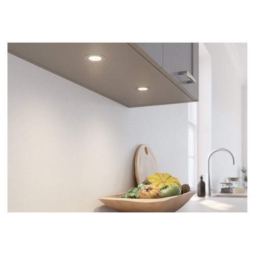 Under cabinet single light in natural white, featuring a sleek design with a circular shape, mounted on a grey kitchen surface above a wooden bowl of colorful vegetables.