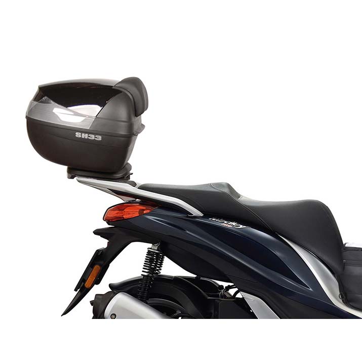 Black Top Master Topcase Fitting by Shad, featuring a sleek design, mounted on a scooter with a smooth seat and visible rear suspension.