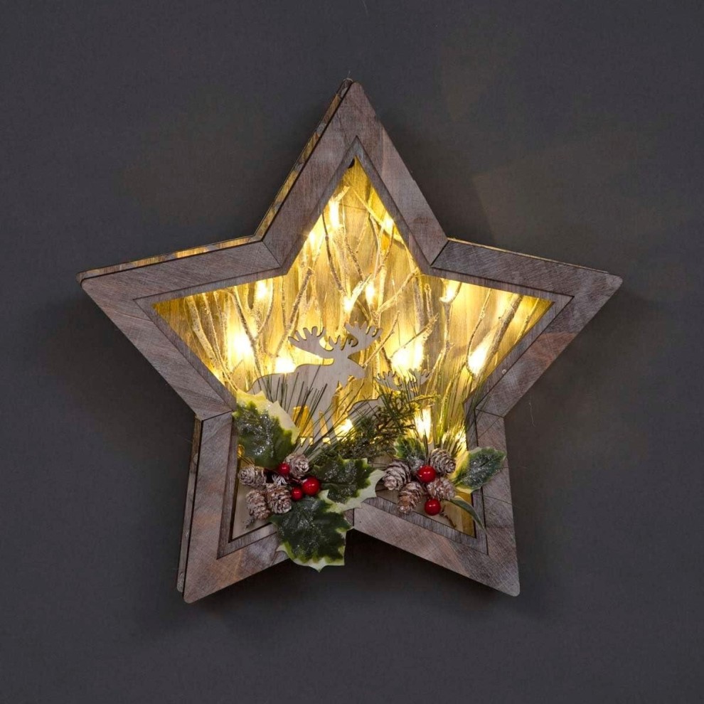Wooden star-shaped tabletop decor featuring a reindeer silhouette, illuminated by warm LED lights, adorned with greenery, pinecones, and red berries for a festive touch.