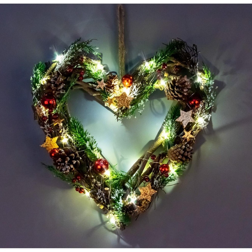 A heart-shaped hanging decoration made of twigs, adorned with red and brown accents, pinecones, and stars, illuminated by warm LED lights.