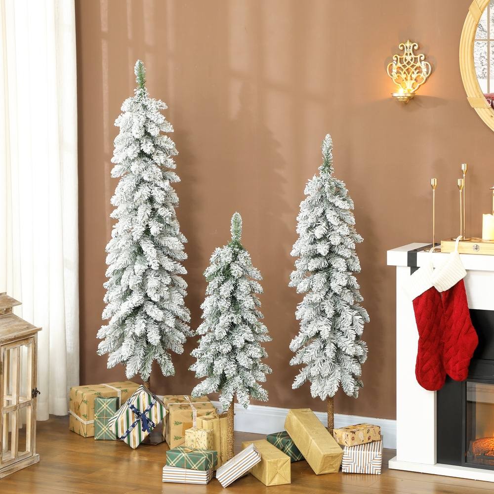 Set of 3 green flocked Christmas trees in varying heights, featuring downswept branches, with a snowy finish, placed near a fireplace and wrapped gifts.
