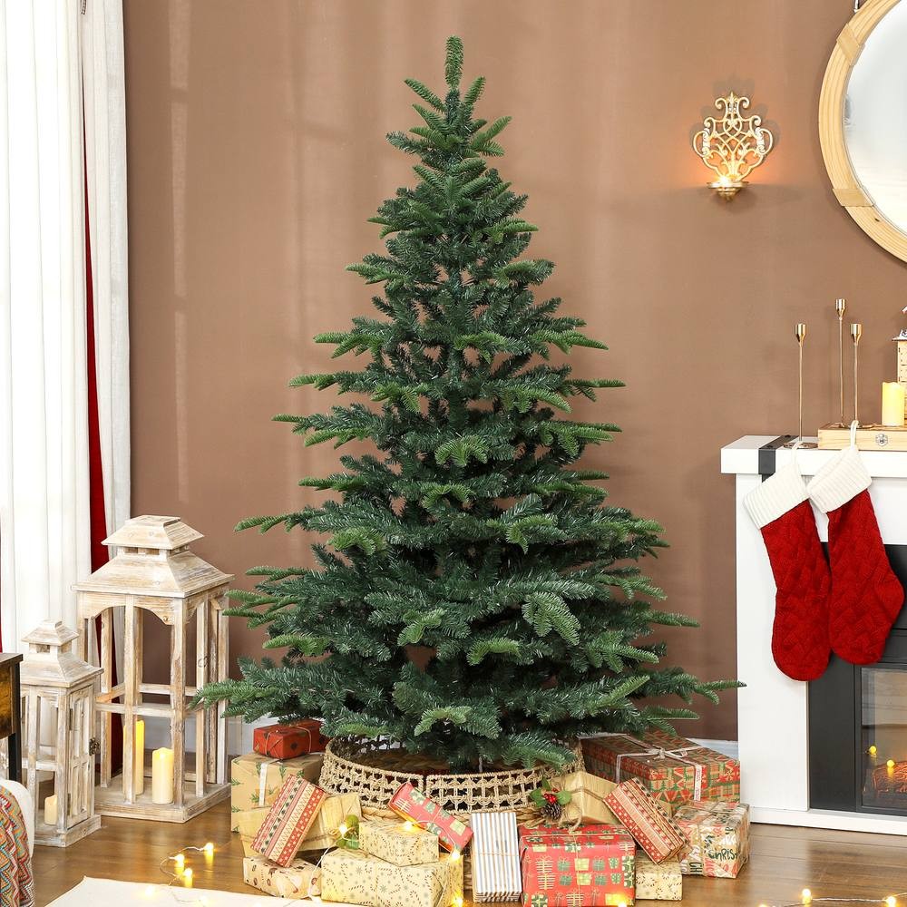 6ft green hinged Christmas tree with realistic branches, set against a brown wall, surrounded by wrapped gifts and decorative lanterns, with stockings hanging nearby.