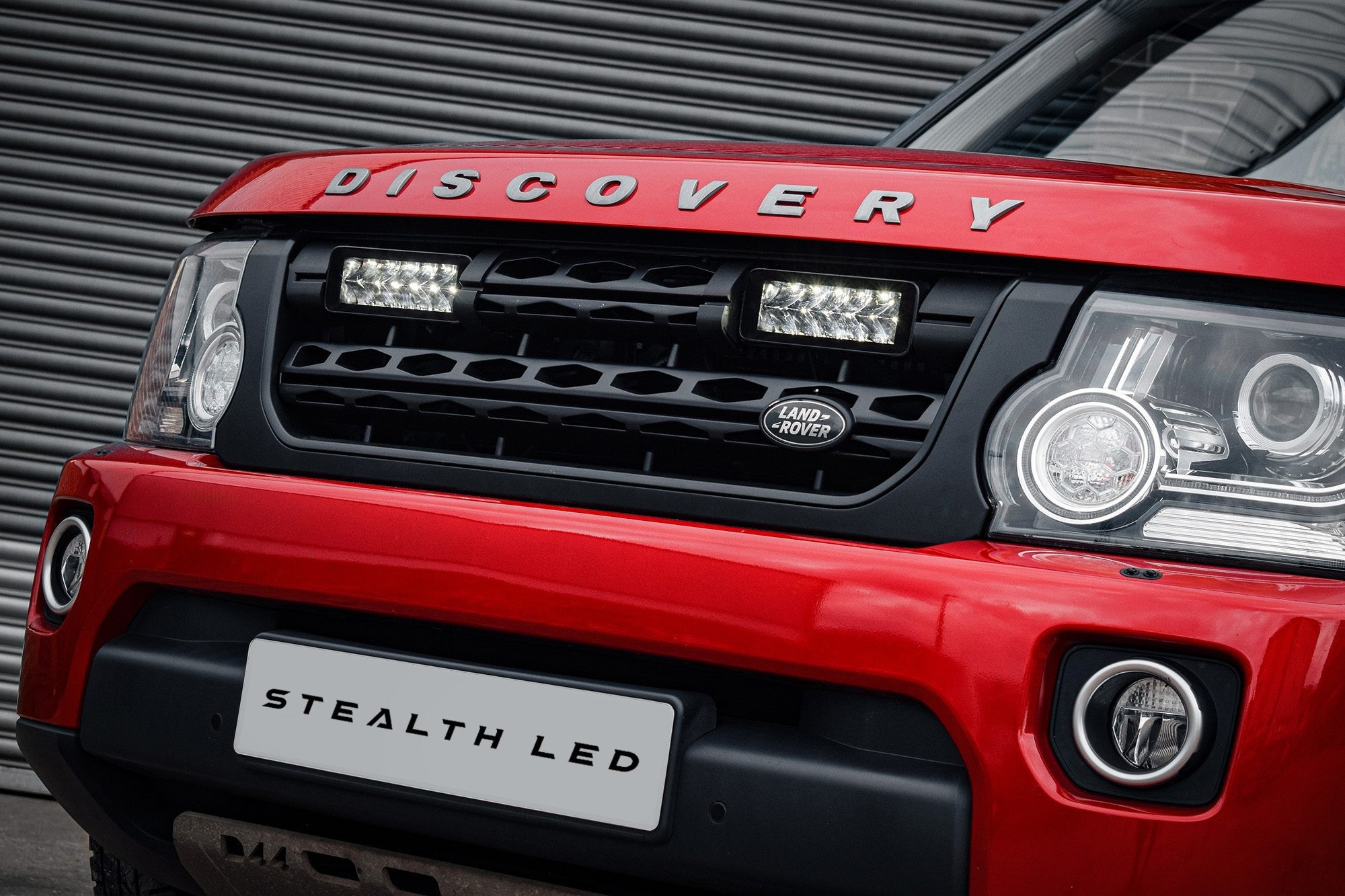 Red Land Rover Discovery 4.5 grille featuring a black integration kit with twin 7" luminous LED lights, prominently displaying "DISCOVERY" in silver lettering above.