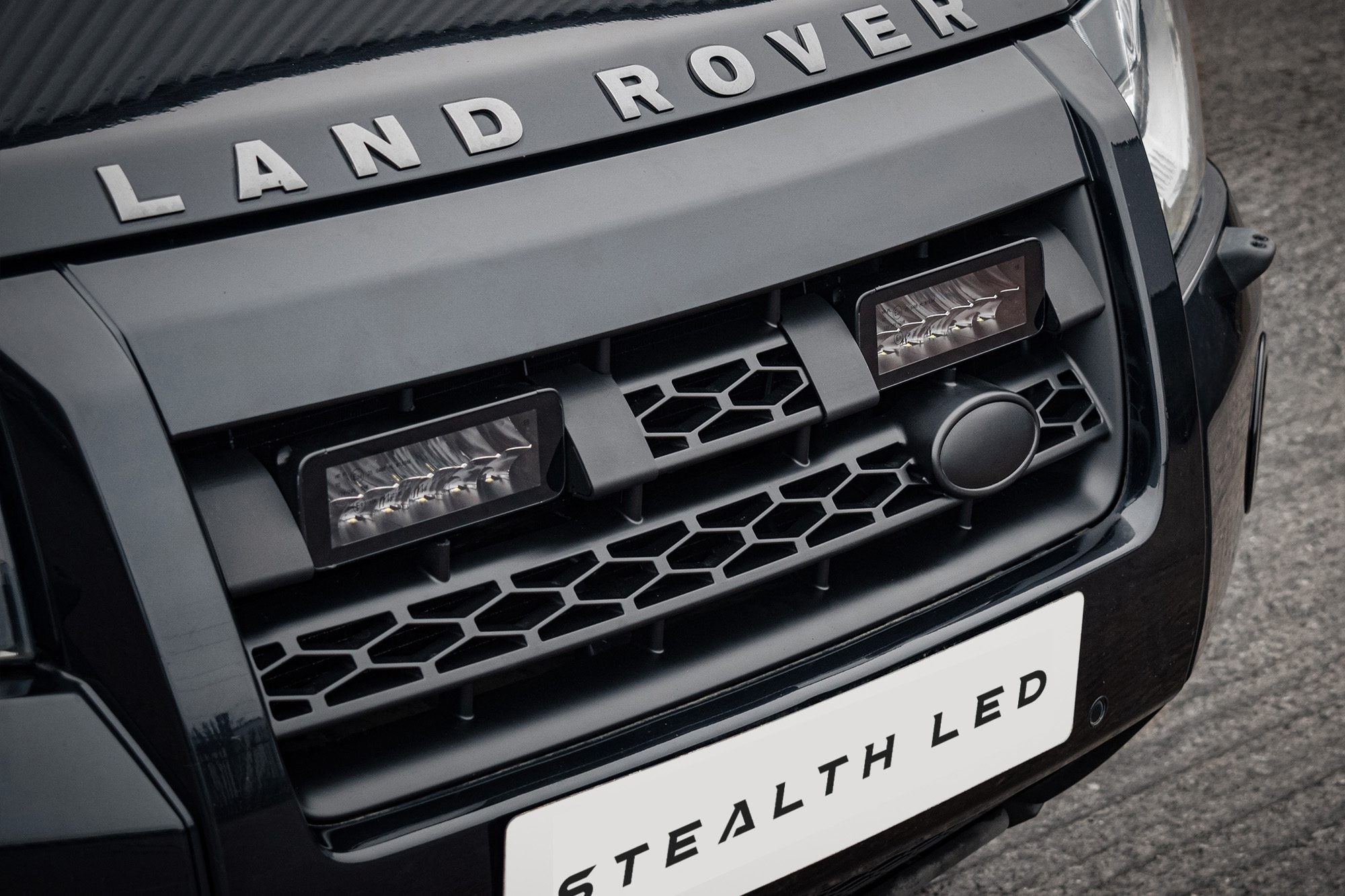 Black front grille of a Land Rover Freelander 2 featuring the "Stealth LED" logo, with two twin 7" luminous LED lights integrated into the design, showcasing a sleek, modern look.