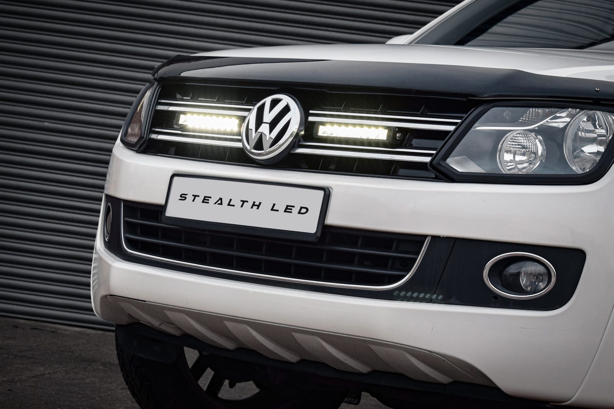 Black and chrome grille kit for VW Amarok (2010-2016) featuring two 10" luminous LED lights, with a sleek design and a white vehicle background.
