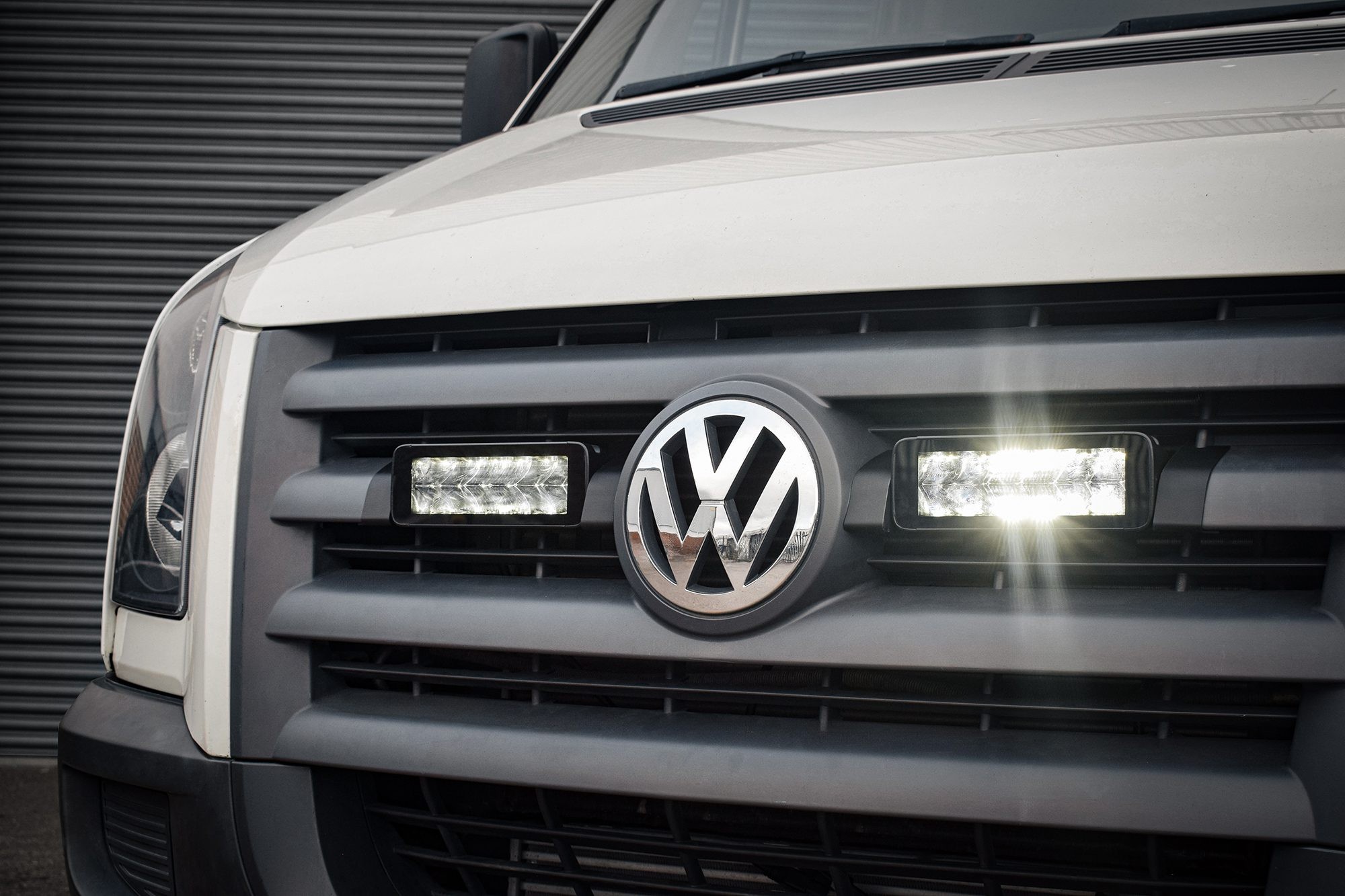 Stealth LED integration kit featuring two 7-inch luminous LED lights, mounted on a black grille of a VW Crafter, emitting bright white light.