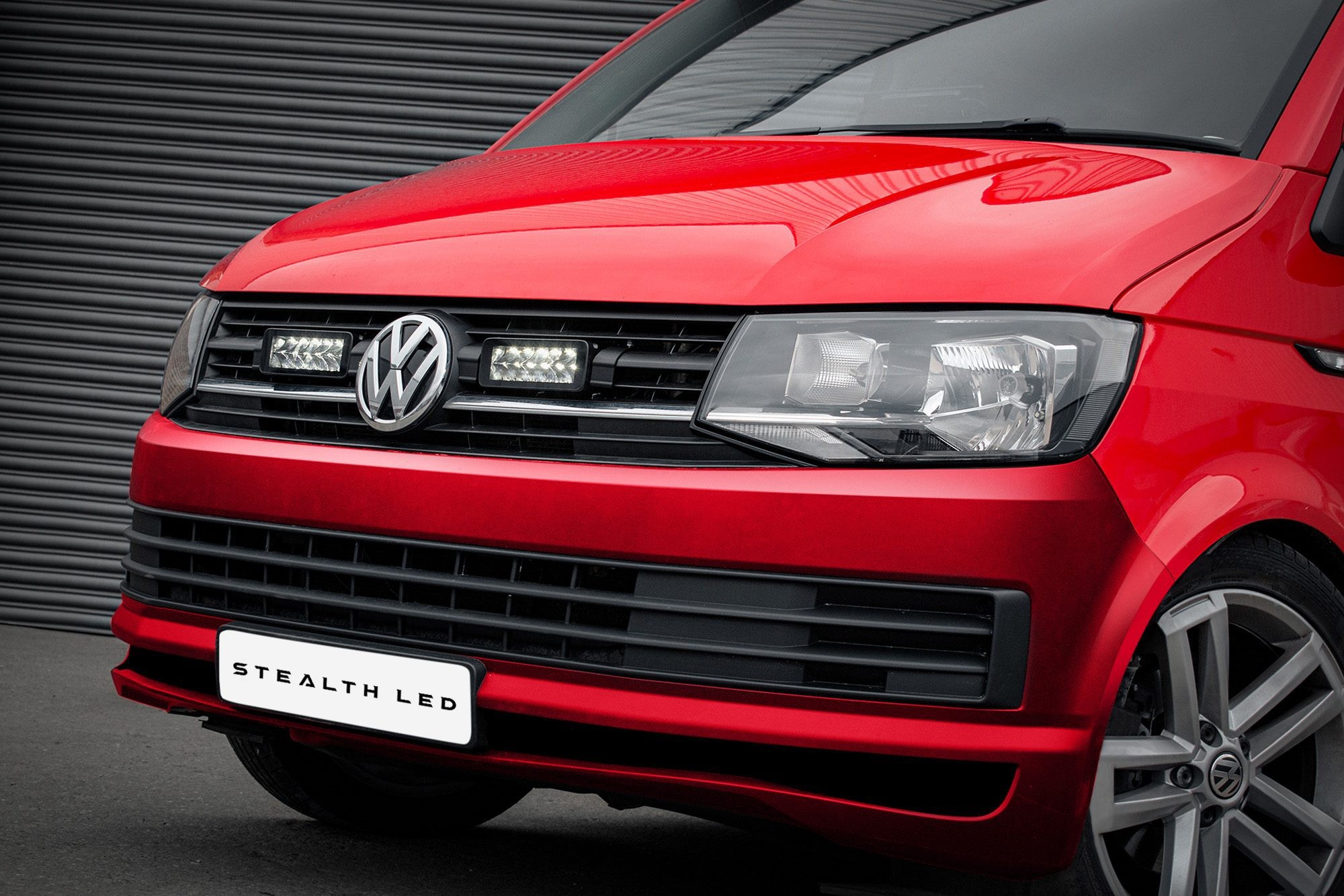 Red Volkswagen Transporter T6 with a sleek front design, featuring twin 7" luminous LED lights integrated into the grille, showcasing a modern and sporty appearance.