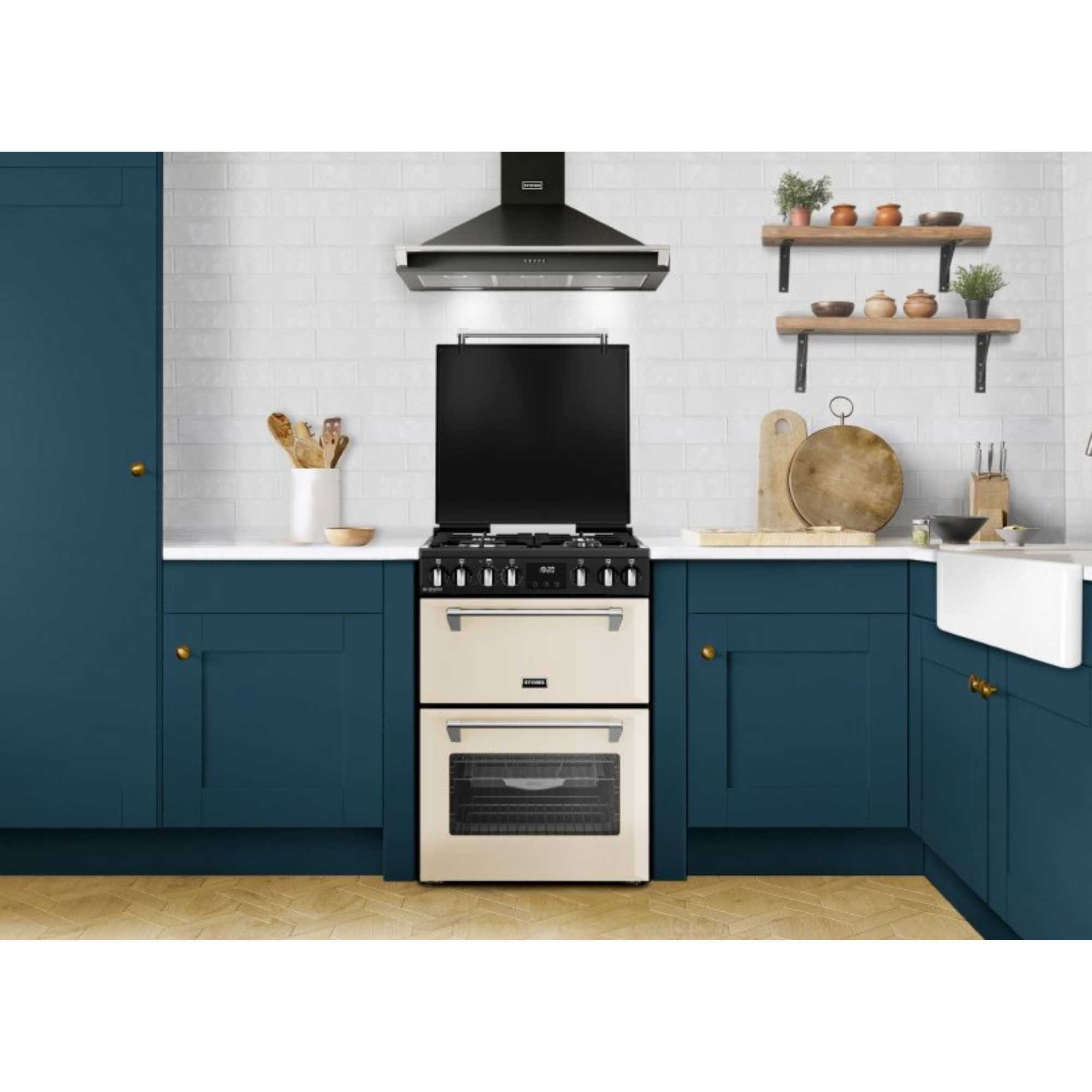 Cream-colored Stoves Richmond DX 60cm dual fuel cooker with six burners, a large oven, and a sleek design, set against a modern kitchen backdrop with navy cabinets and wooden shelves.