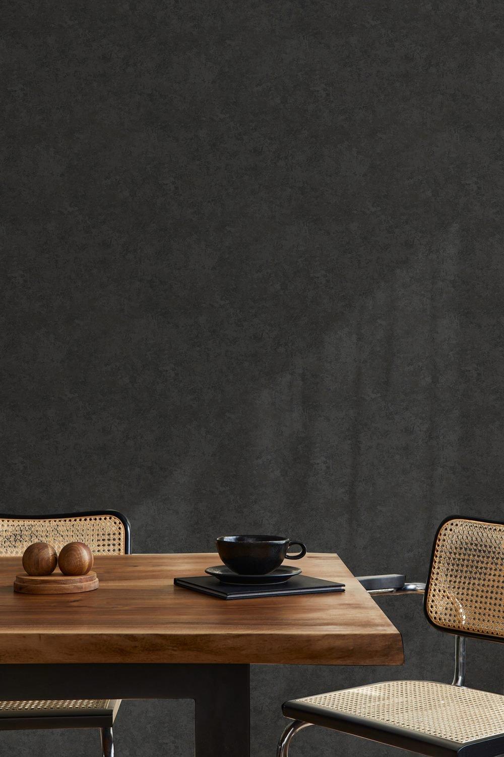 Textured black wallpaper with an organic finish, featuring a subtle pattern, complements a wooden table with a black cup and decorative wooden orbs on a dark plate.