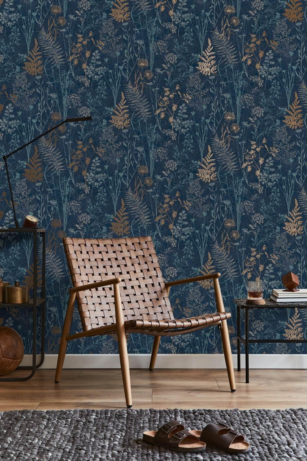 Dark navy floral wallpaper featuring metallic sage and gold accents, with a botanical pattern of ferns and flowers, complemented by a wooden chair and textured rug in a cozy setting.