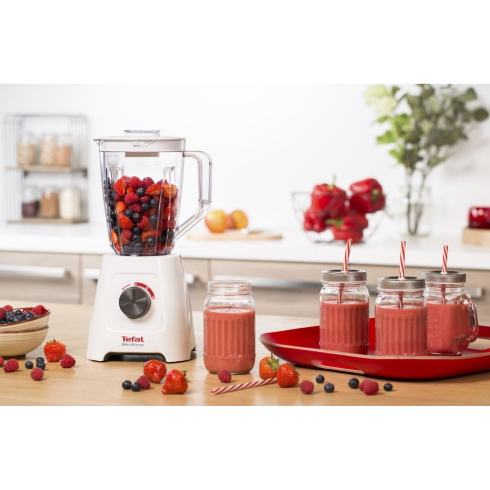 Tefal Blendforce II blender in white with a transparent plastic jug, filled with berries, alongside jars of pink smoothies and a red serving plate with strawberries and blueberries.