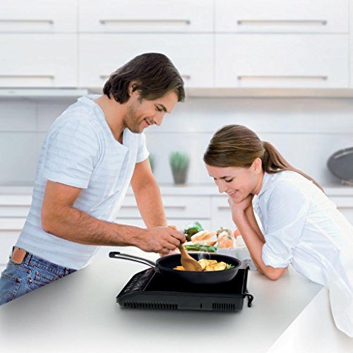 Black Tefal IH201840 Everyday Induction Portable Hob on a kitchen countertop, featuring a sleek design, digital controls, and a cooking pan with food being prepared by a man and woman.