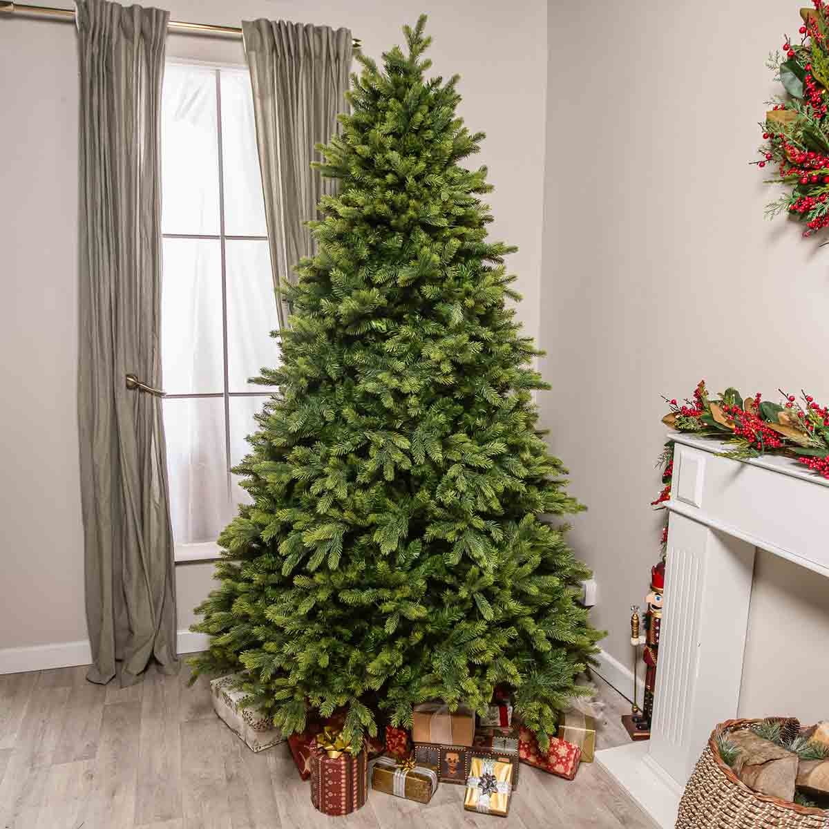 7.5FT green artificial PE Christmas tree with lush branches, placed in a corner near a window, surrounded by wrapped gifts and decorative elements.
