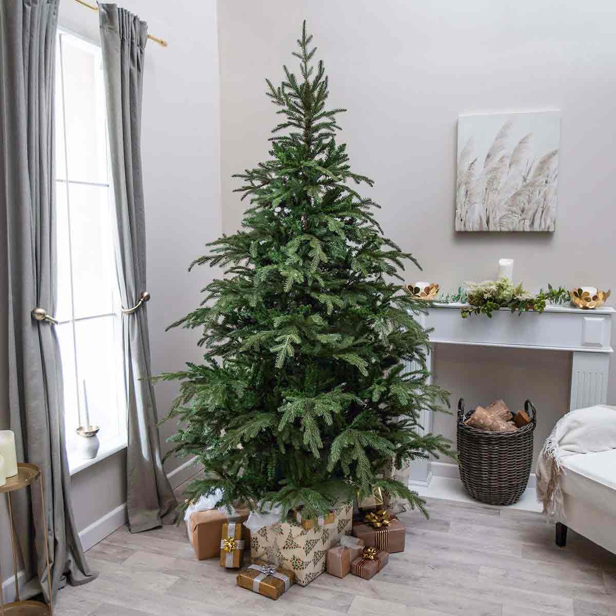 6ft Highclere artificial spruce Christmas tree in green, featuring realistic branches, set in a cozy room with wrapped presents beneath and decorative elements nearby.