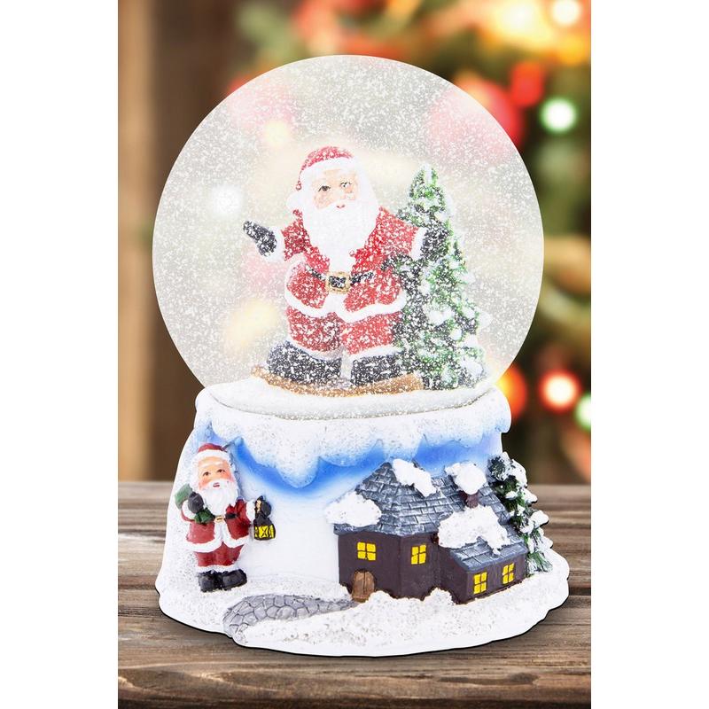 A festive snow globe featuring a cheerful Santa in a red suit, surrounded by snow, with a detailed winter village scene on the base, including a small house and a child holding a lantern.