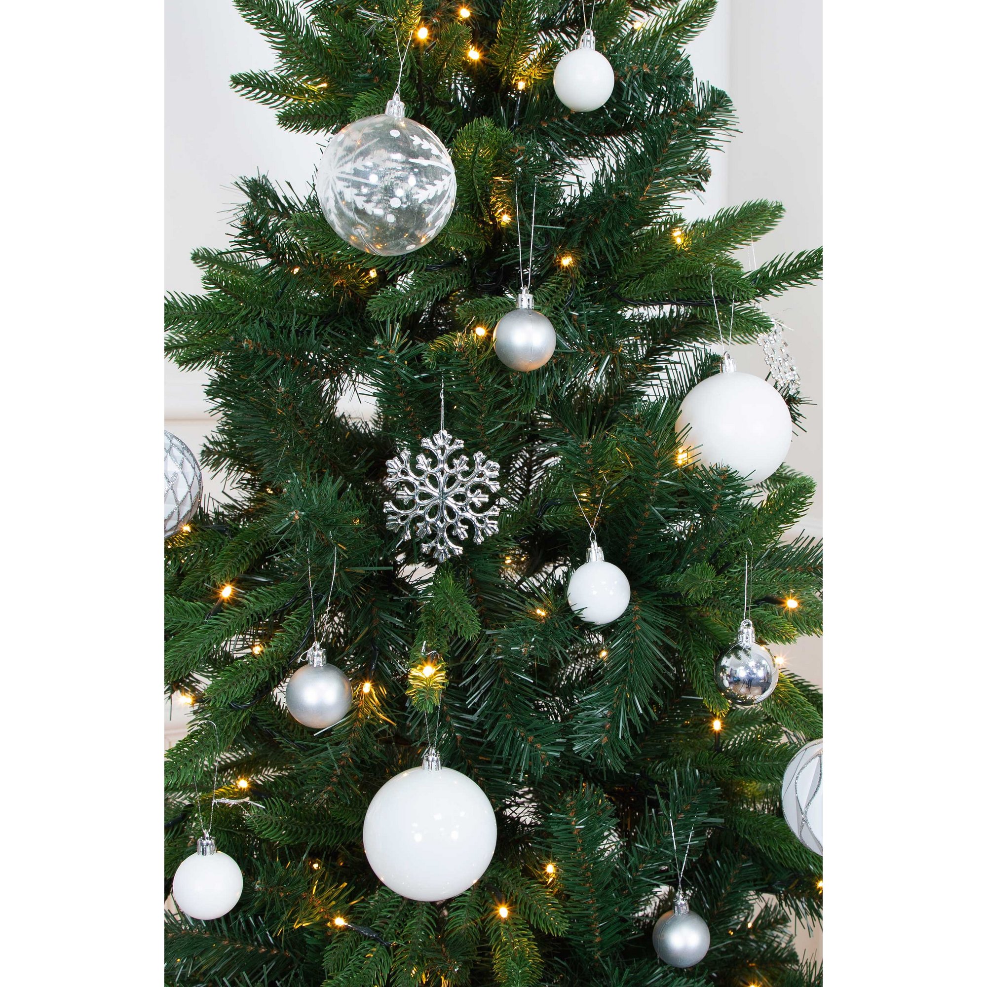 A Christmas tree adorned with a variety of white and silver shatterproof baubles, including matte and shiny finishes, alongside a decorative snowflake ornament.