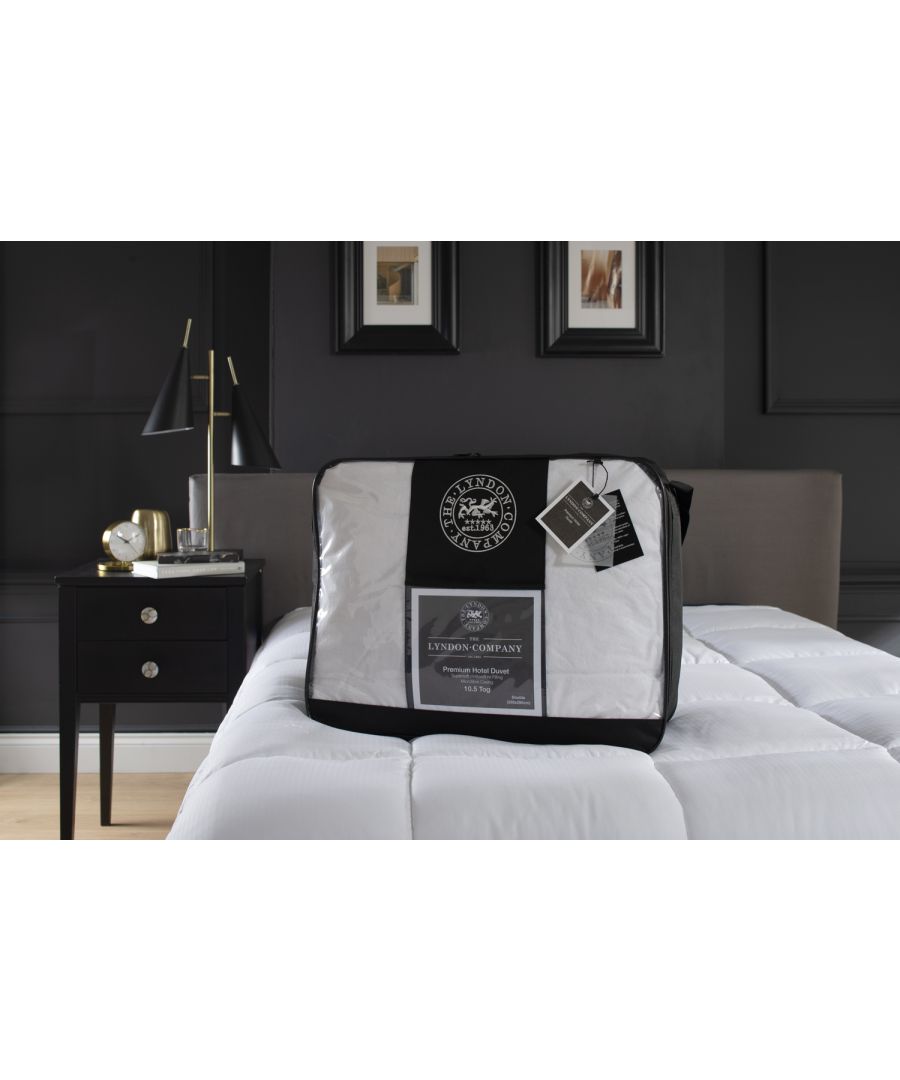 Premium soft touch 10.5 tog duvet in a clear packaging bag, featuring a black trim, displayed on a bed with a dark wall background and a bedside table with a lamp.