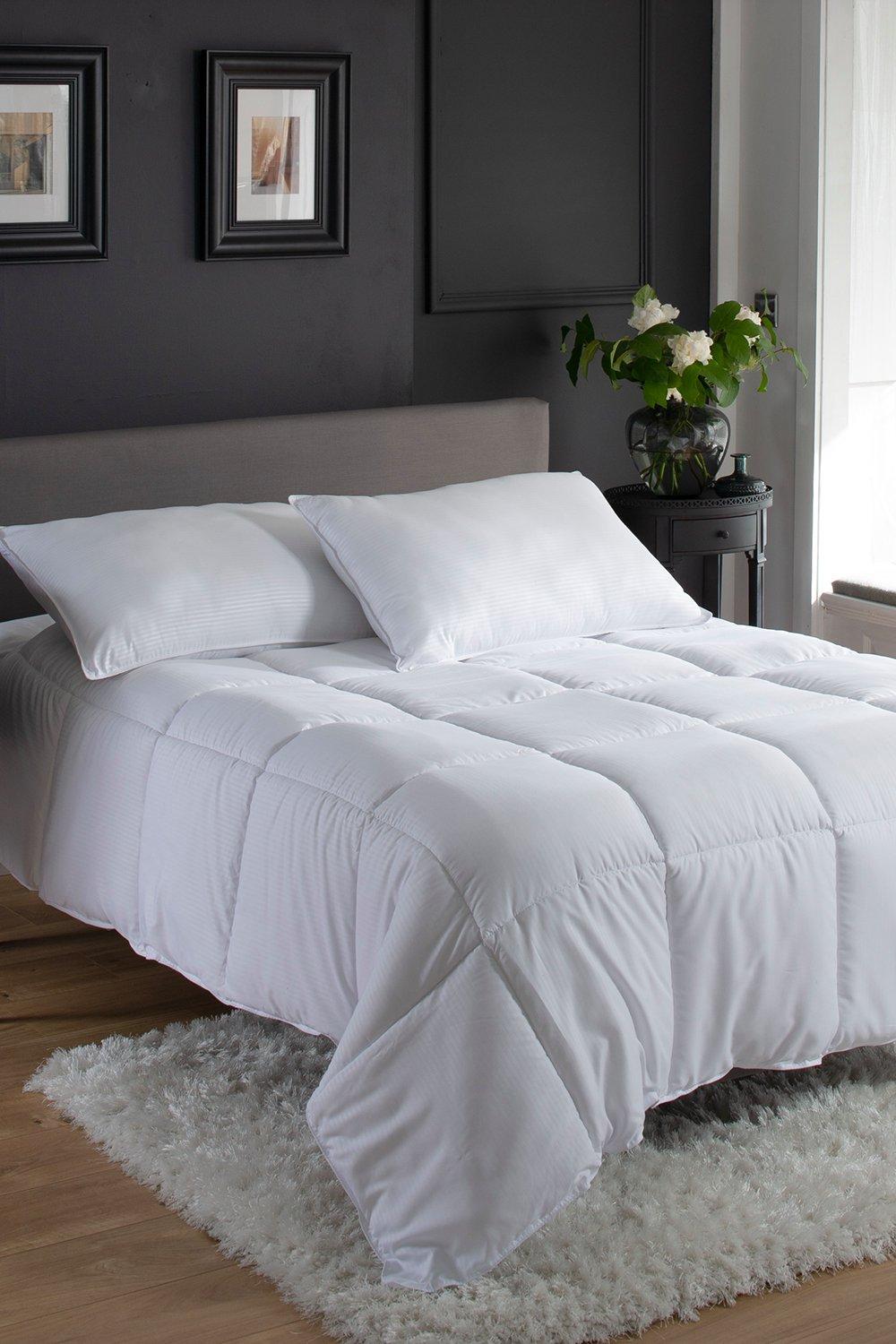 White 10.5 tog duvet on a double bed, featuring a soft, quilted design, paired with two matching white pillows, set against a dark wall and a decorative plant.