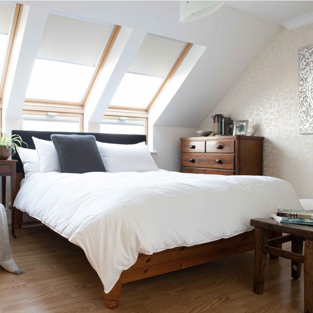 White 13.5 Tog duvet with a 240 thread count casing on a wooden bed, complemented by dark grey and white pillows, in a bright, modern bedroom with slanted skylights.