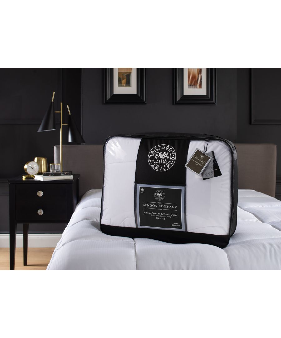 White 10.5 tog duvet by The Lyndon Company, made of goose feather and down, displayed in a black and white packaging on a bed beside a stylish lamp and nightstand.