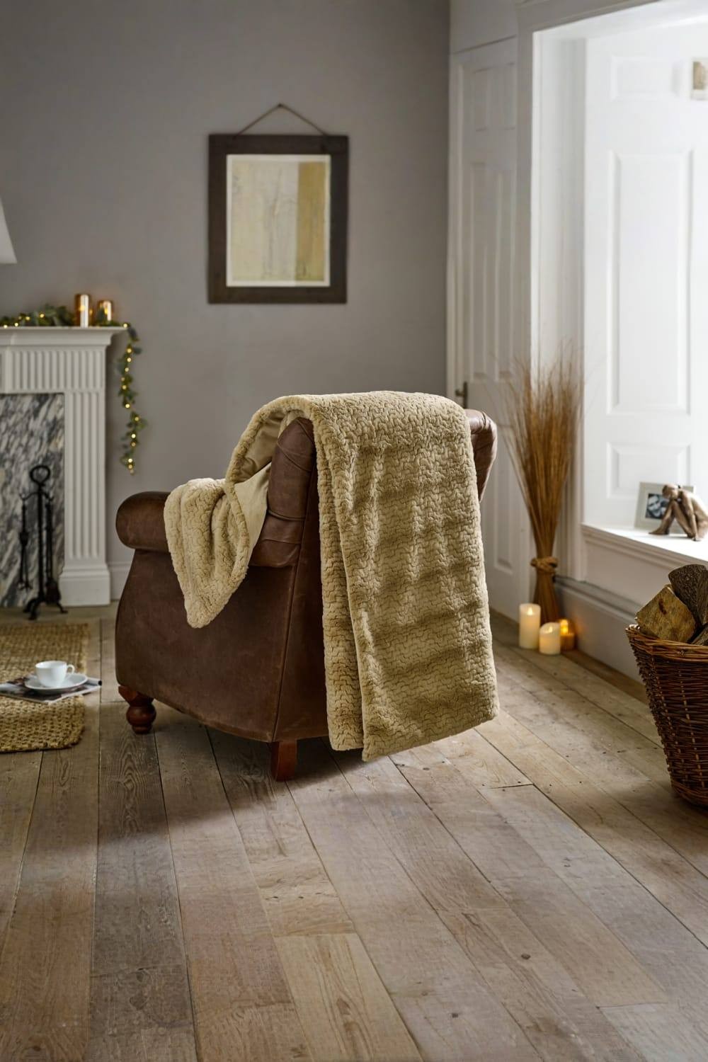 Cream faux fur throw draped over a brown leather armchair, featuring a soft, textured surface, measuring 130x170cm, set in a cozy, warmly lit living room.