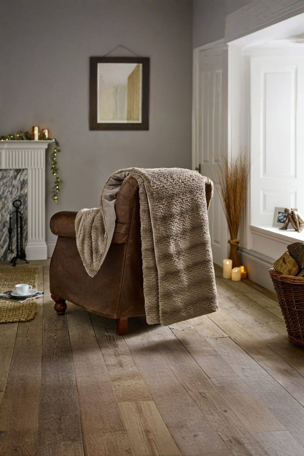 Soft fawn faux fur throw, measuring 130x170cm, draped over a brown leather armchair, set in a cozy room with wooden flooring and warm lighting.