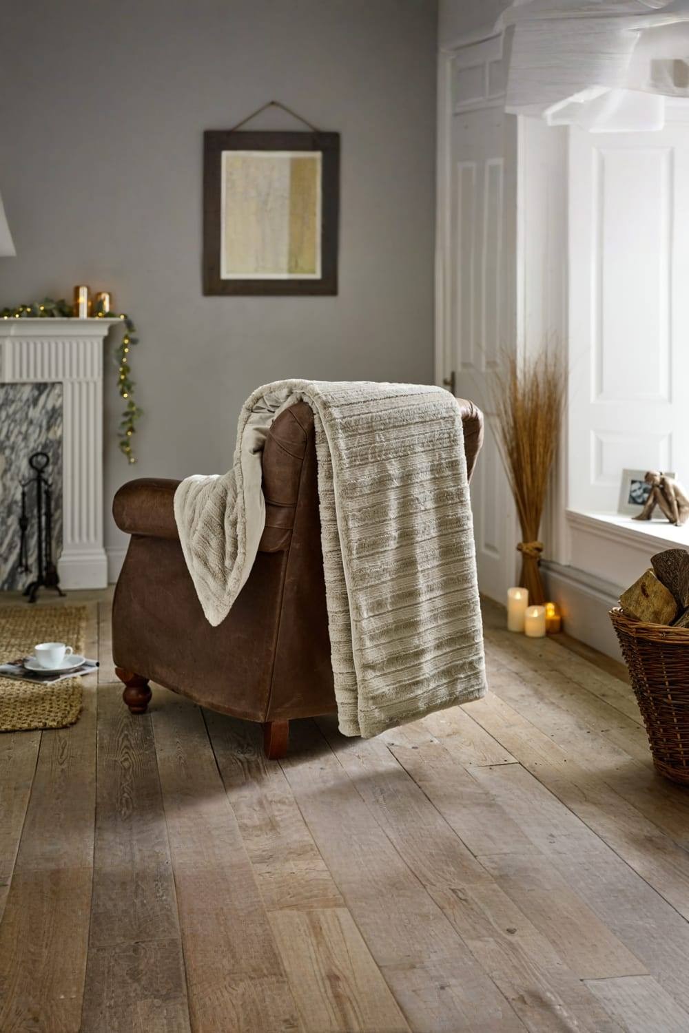Soft faux fur throw in fawn draped over a brown leather armchair, featuring a textured design, set in a cozy room with wooden flooring and warm lighting.