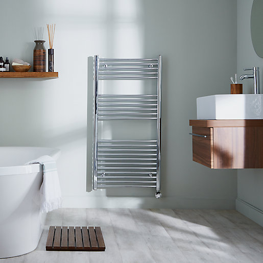 Chrome electric towel warmer with a sleek, modern design, featuring multiple horizontal bars, mounted on a light-colored wall beside a wooden vanity and bathtub.