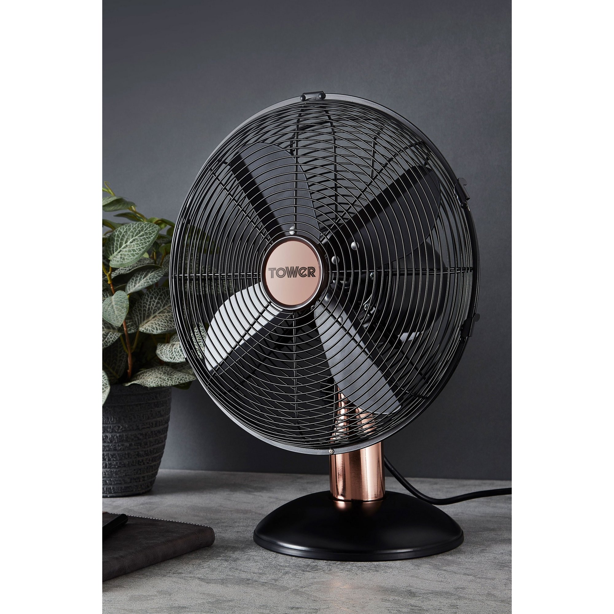 Midnight blue 12-inch metal desk fan by Tower features a sleek design with a copper base, black blades, and a sturdy round stand, perfect for stylish cooling.