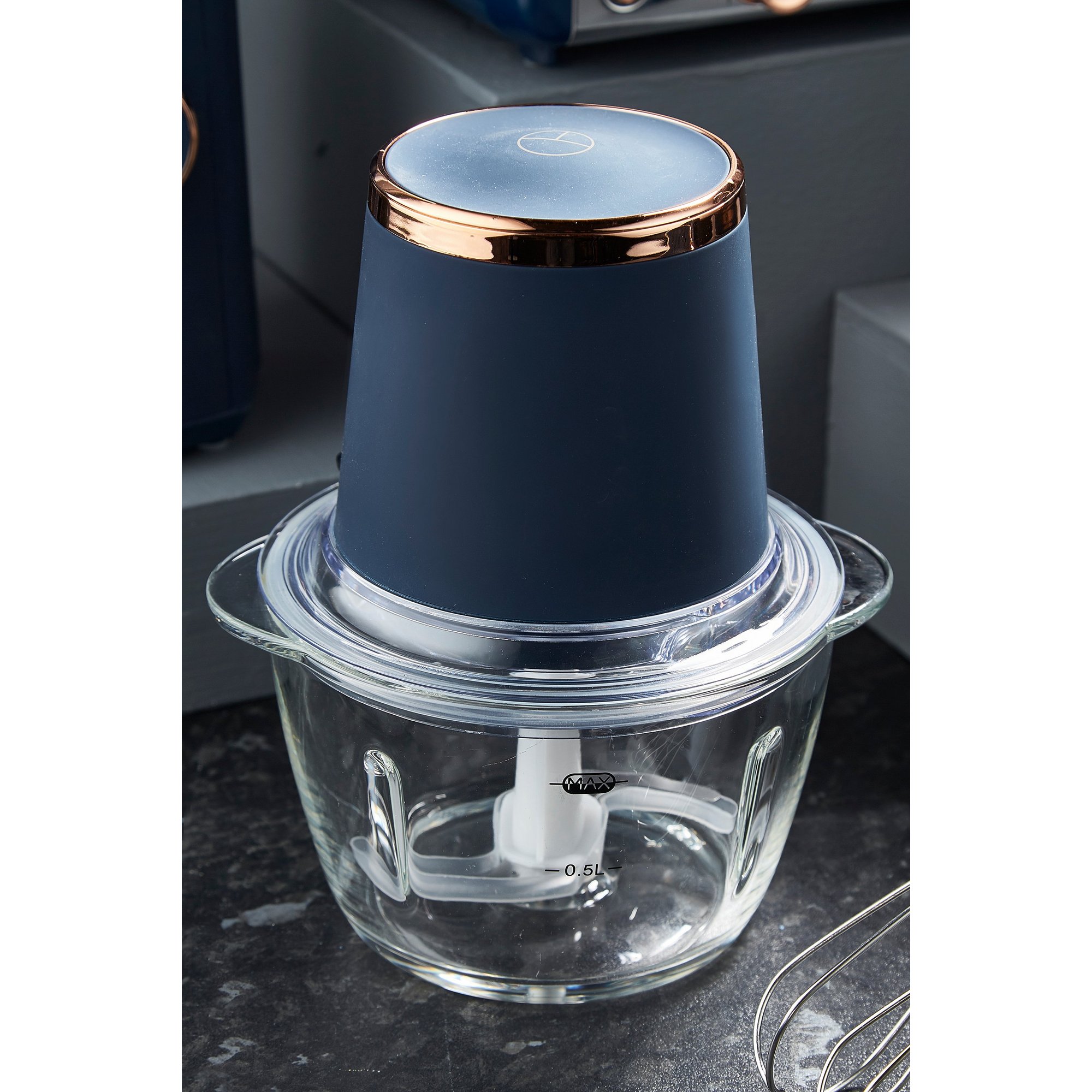 Pink mini chopper with a glass bowl, featuring a white chopping blade and a dark blue lid with a rose gold accent on top.