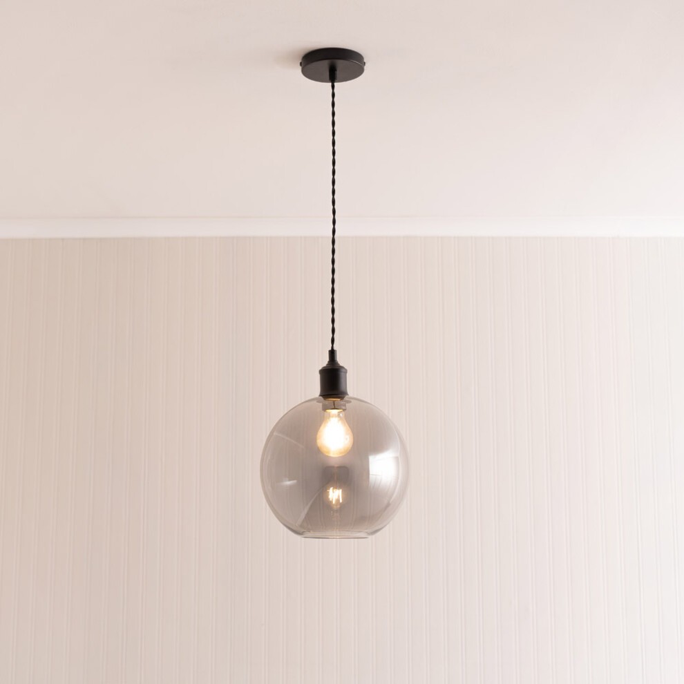 Smoked glass globe pendant light in matte black, featuring a single bulb, suspended from a black braided cord against a light-colored wall.