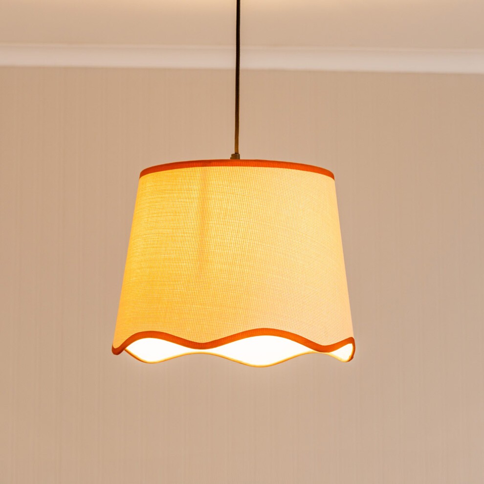 Burnt orange fabric lamp shade with a scalloped edge, featuring a textured surface and contrasting trim, suspended from a ceiling fixture.