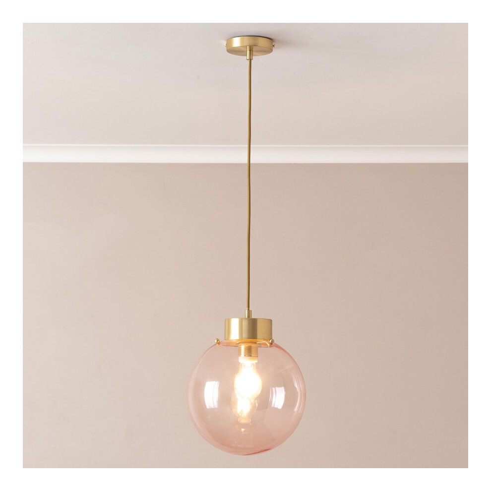 Frenchie pink glass globe ceiling pendant light with a brushed gold cap, featuring a visible bulb inside, suspended from a gold cord against a neutral background.