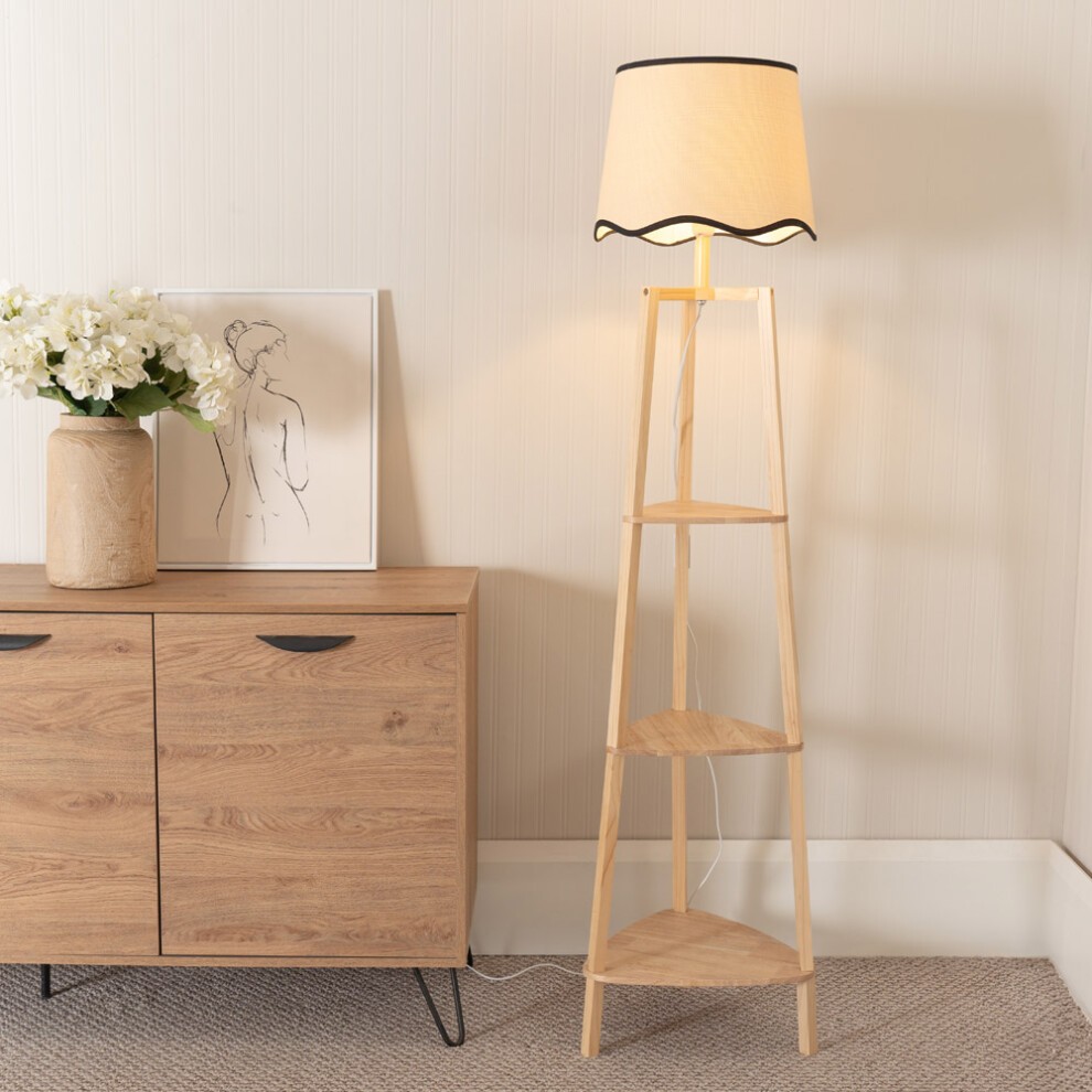 Black floor lamp with a scallop shade, wooden three-tier shelf design, and a light bulb, placed beside a wooden cabinet and a framed artwork with flowers.