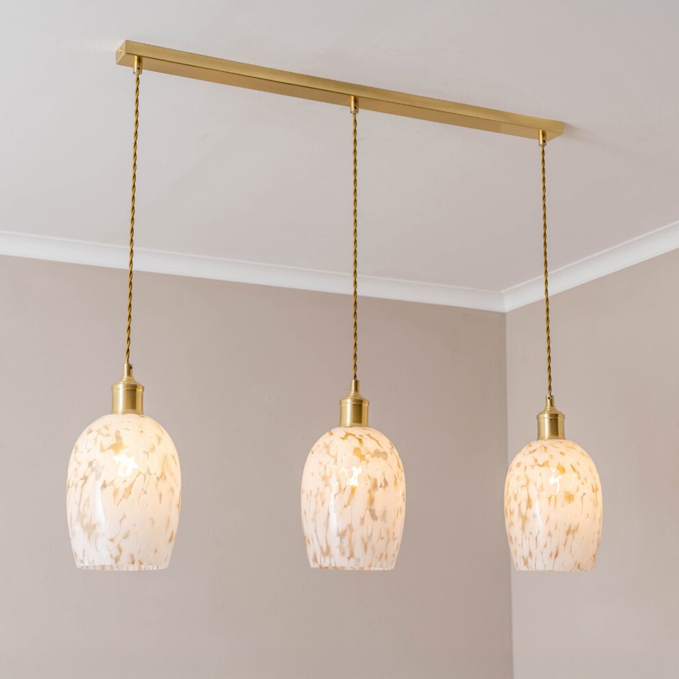 Three gold diner ceiling pendant lights with confetti glass shades, featuring a marbled white and gold design, suspended from a sleek gold bar.