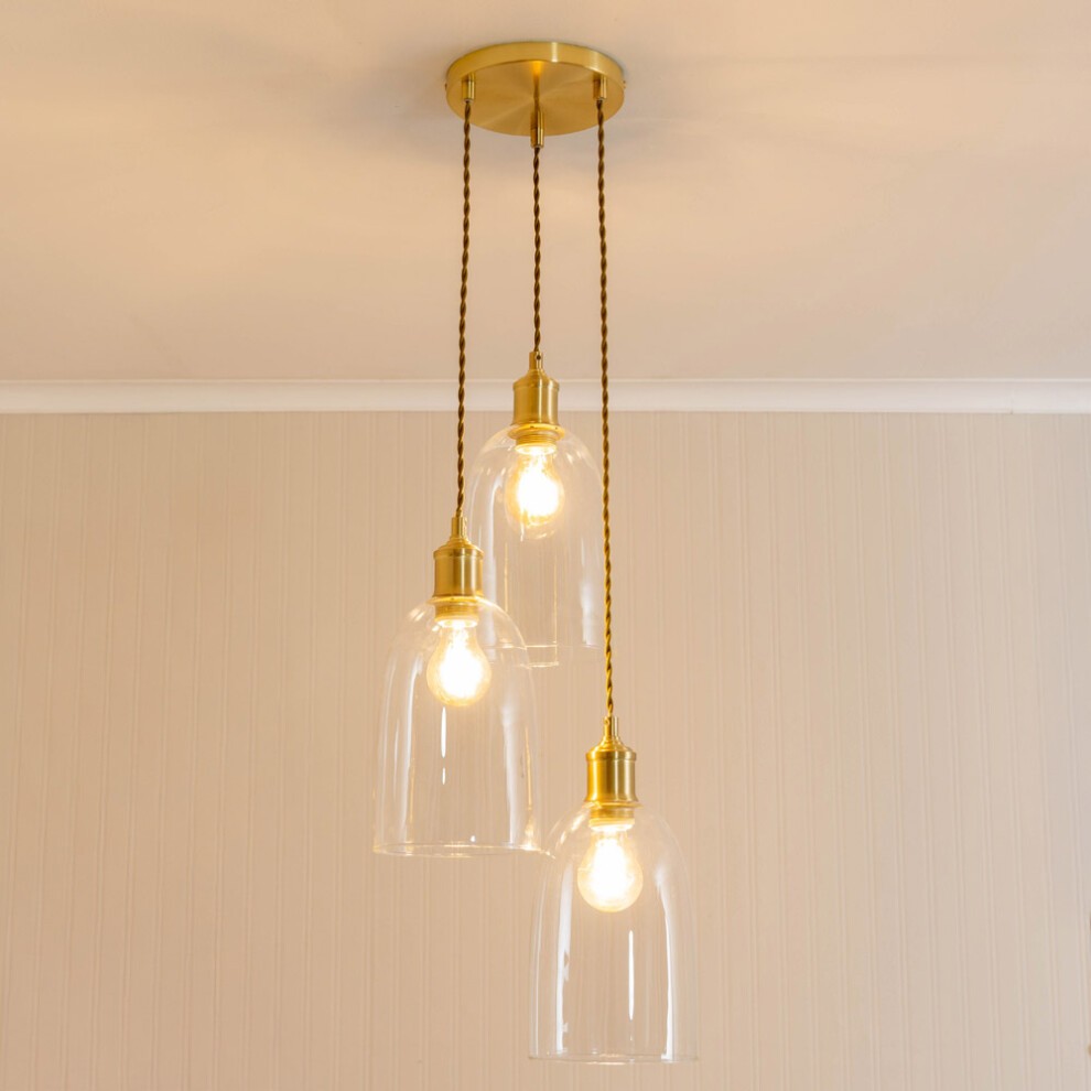 Gold ceiling pendant light featuring three glass cloche domes with LED bulbs, suspended by twisted cords from a circular ceiling mount.