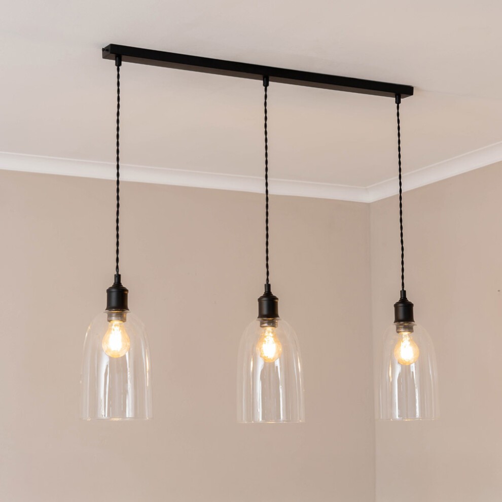 Three glass cloche dome pendant lights hang from a black bar, featuring LED bulbs and black fittings, set against a neutral wall.