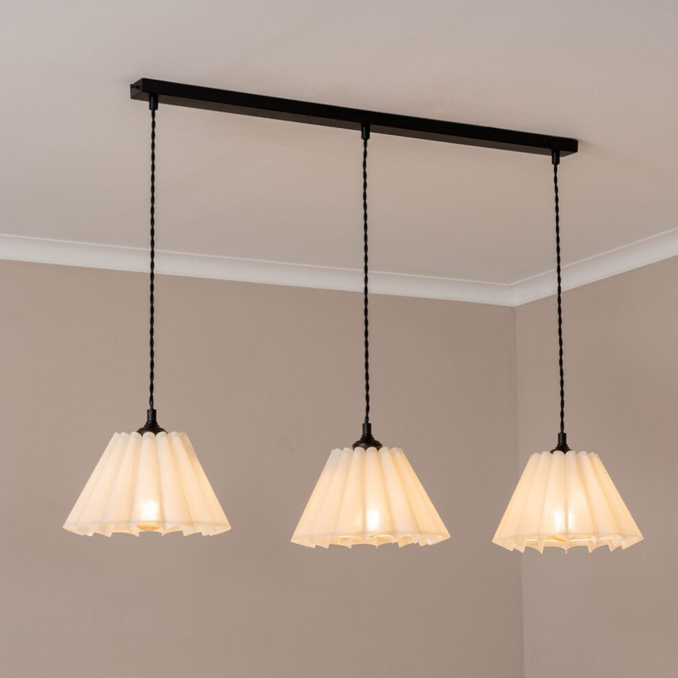 Three white pleated lampshades hang from a matte black bar, featuring a modern diner style, with soft light bulbs illuminating the space.