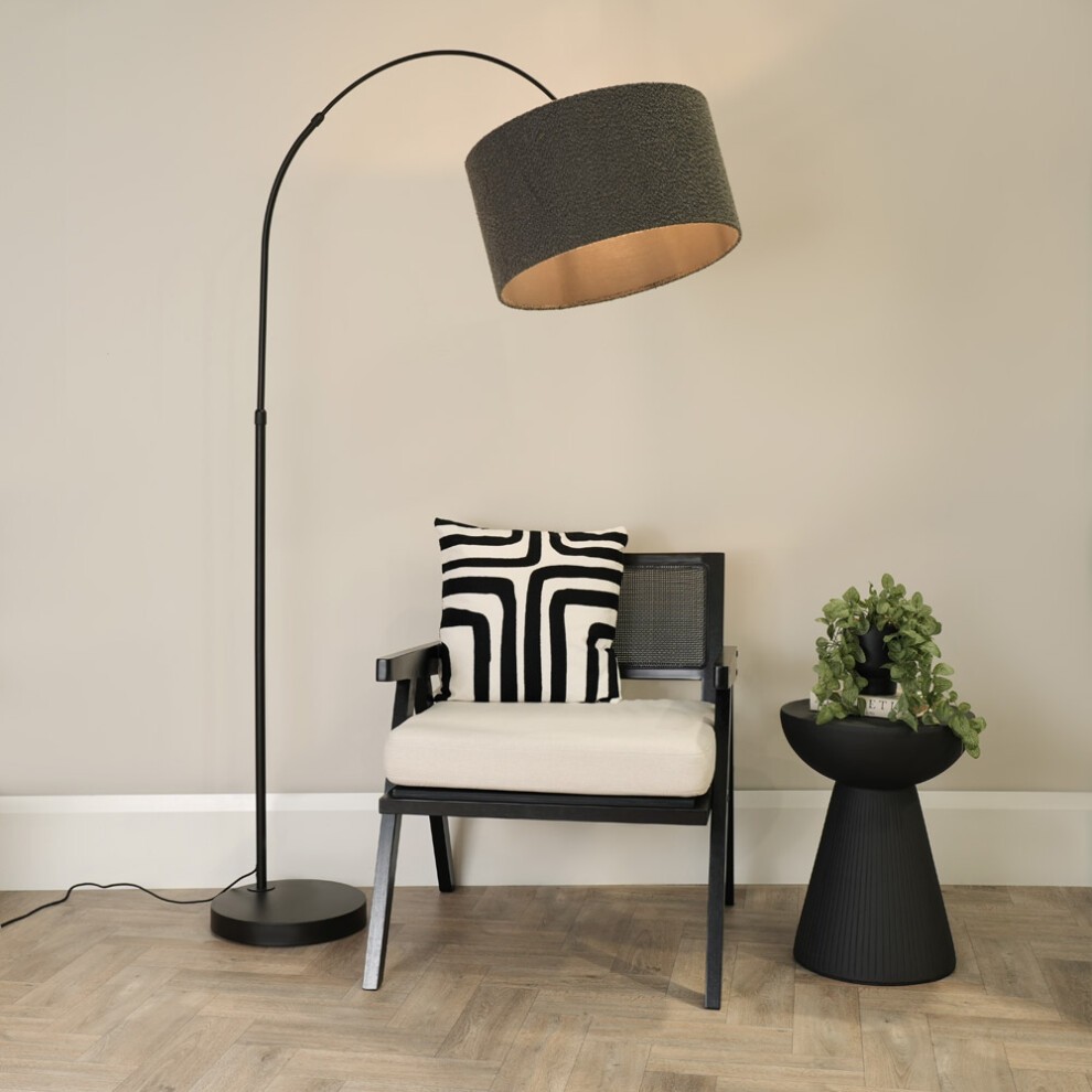Black arched floor lamp with a boucle drum shade in charcoal, paired with a modern chair featuring a black and white patterned cushion and a round side table with greenery.