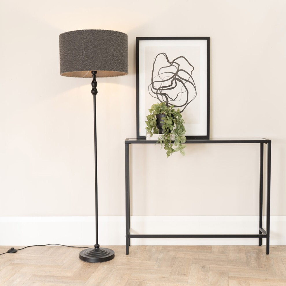 Maggie Black Candlestick Floor Lamp features a sleek black metal base, a charcoal boucle lamp shade, and an LED bulb, positioned beside a minimalist console table and artwork.
