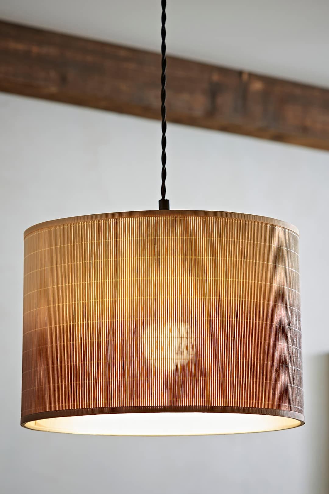 Brown ombre bamboo drum pendant lamp shade with a textured finish, featuring a warm glow from the light source inside, suspended by a black cord.