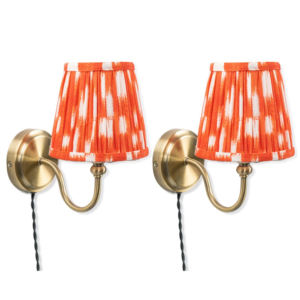 Pair of antique brass wall lamps with orange pleated tapered shades featuring a white brushstroke pattern, mounted on curved arms with black cords.