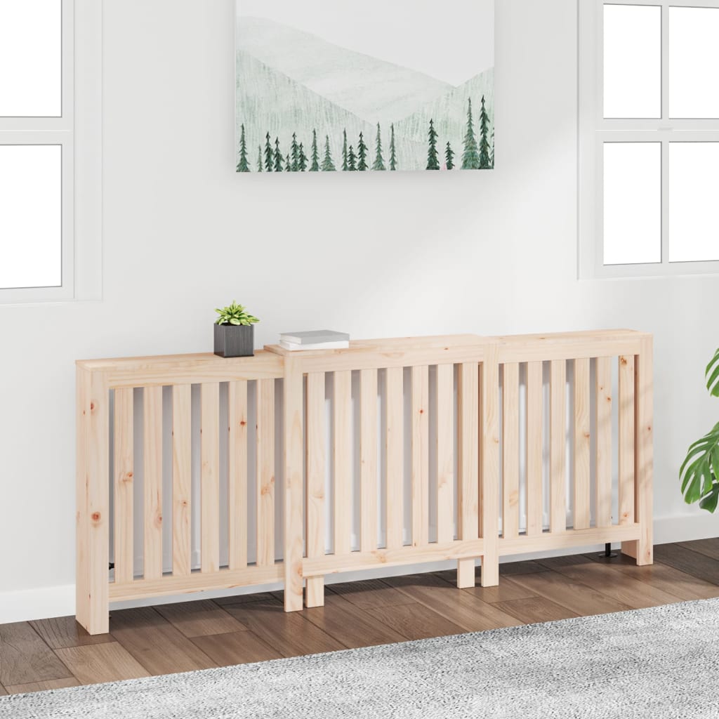 Solid wood pine radiator cover in a natural finish, featuring slatted design, positioned against a white wall with a small plant and books on top, and a mountain-themed artwork above.