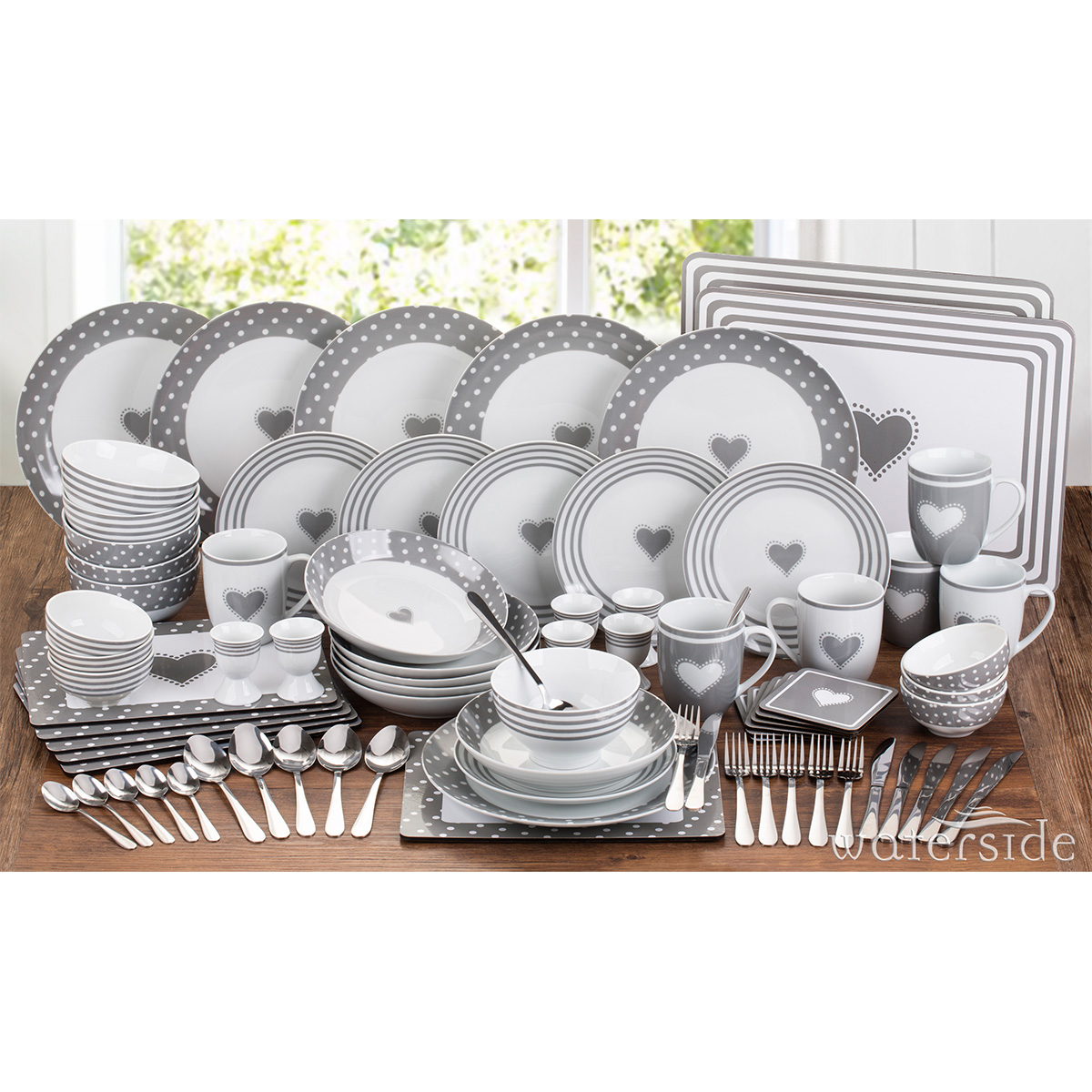 An 80-piece dinner set featuring grey plates, bowls, and mugs adorned with white heart designs, complemented by matching cutlery and placemats.