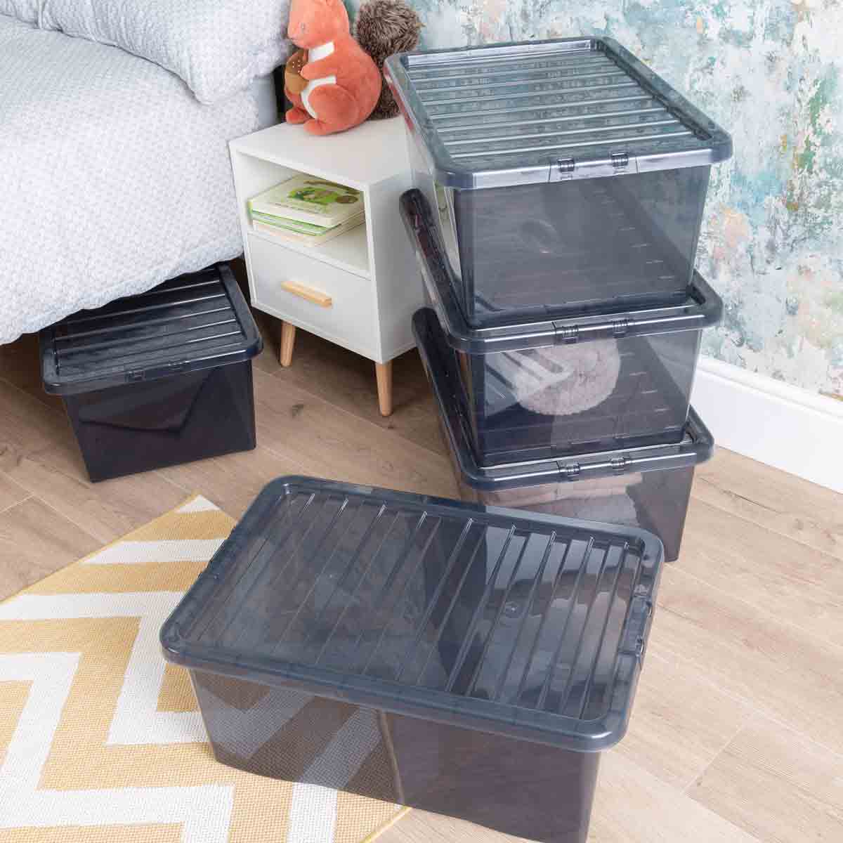 Three black Wham Crystal Tint Smoke storage boxes with lids stacked beside a bed, featuring transparent sides and ribbed lids, ideal for organizing items.