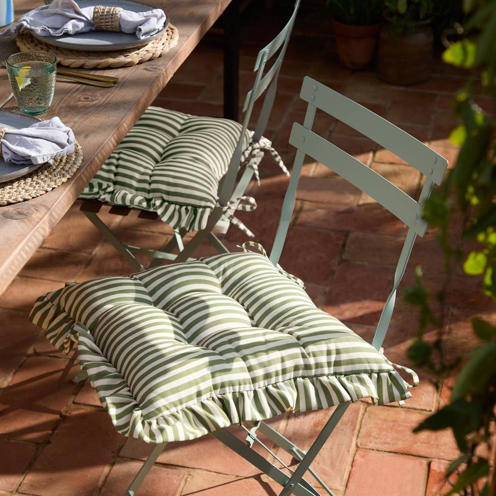 Green striped ruffle seat pads with tufted design, perfect for indoor or outdoor use, placed on light blue folding chairs at a rustic wooden table.