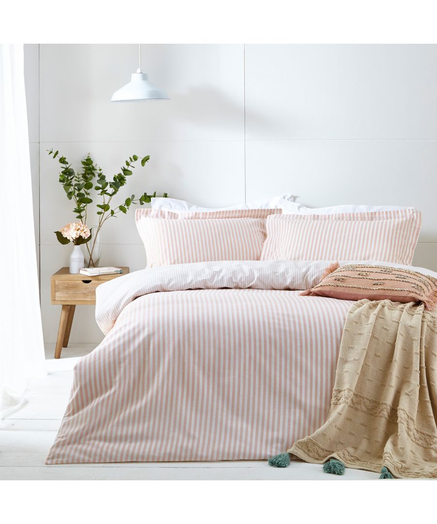 Blush cotton reversible duvet cover set featuring subtle stripes, complemented by matching pillowcases, styled with a textured throw and greenery in a cozy bedroom setting.
