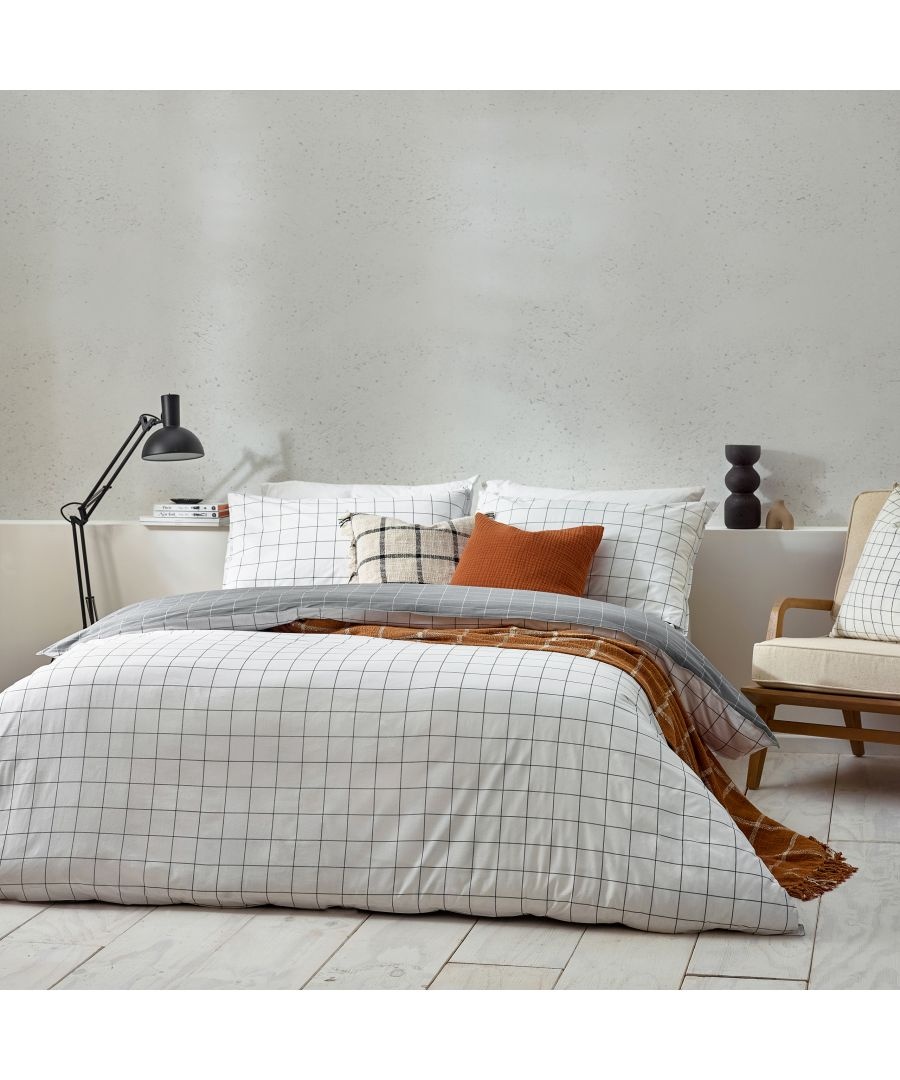 White cotton reversible duvet cover set featuring a black check pattern, paired with textured pillows and a cozy throw, set against a neutral wall and stylish furniture.